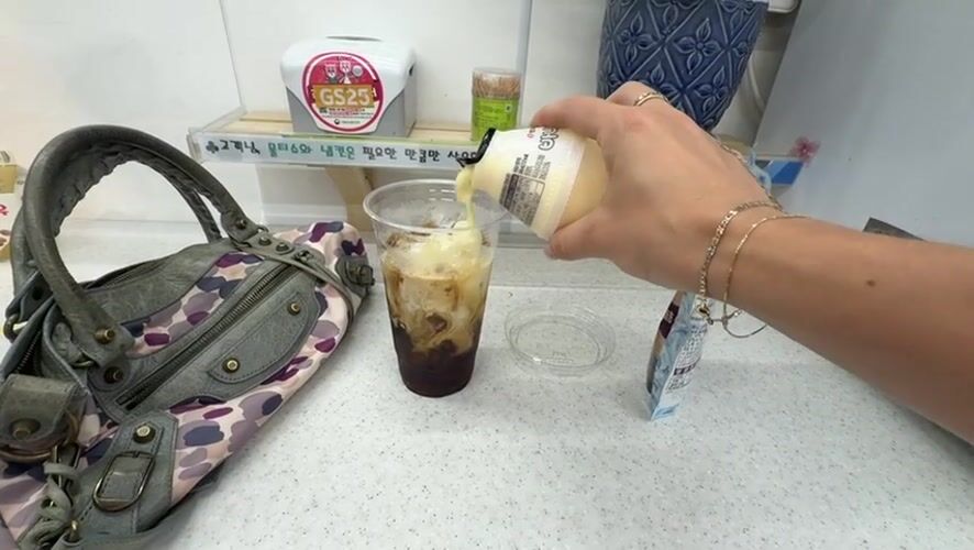 Person adds cream to iced coffee at Seoul convenience store