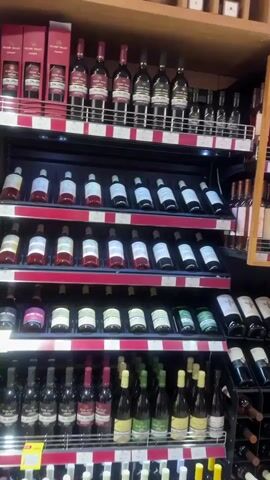 The video shows a store aisle with shelves filled with wine bottles. There are multiple rows of different types and brands of wine, arranged neatly on shelves. The shelves are well-lit, highlighting the various colors and labels of the bottles. The camera slowly pans from left to right, showcasing the extensive selection of wines.