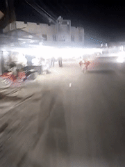 Motorcycle travels lit commercial street in Keudegeudong evening