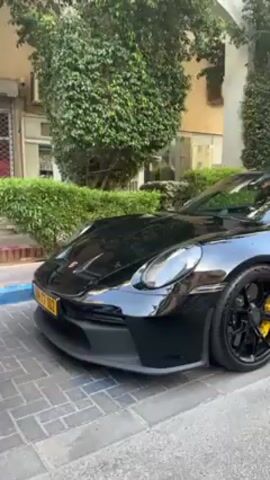 The video shows a black Porsche 911 GT3 parked on a paved street in an urban environment, followed by interior shots from inside a gray Fiat car. The Porsche has yellow brake calipers and a license plate that starts with "77." The Fiat's dashboard has a navigation screen and a steering wheel with the Fiat logo. The Fiat's odometer reads "187488."