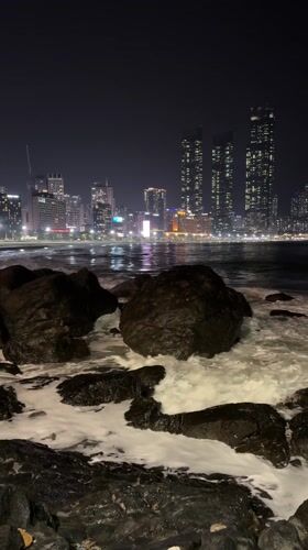 Nighttime beach visitor observes illuminated cityscape in South Korea