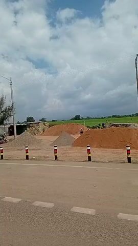 The video shows a road with traffic driving by. In the background, there is construction occurring. The earth is being moved with a tractor. Additionally, there are piles of dirt and other materials in the background of the scene.