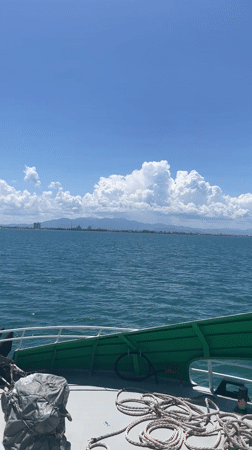 Boat passenger films calm waters, distant cityscape near Vietnam coast