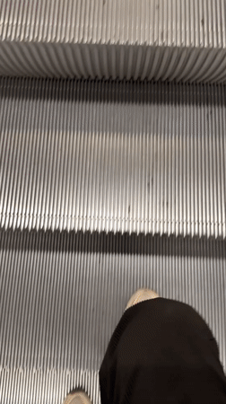 Person ascends escalator in Milan wearing jean jacket