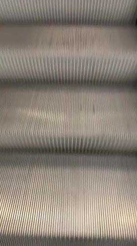 Person ascends escalator in Milan wearing jean jacket
