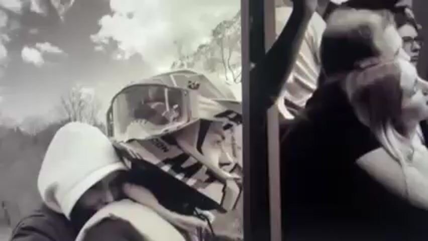 The video appears to be a music video or a visual montage set to music. The video is divided into a series of frames. The first frame shows a black and white image of a person in a motorcycle helmet with another person leaning close, set against a backdrop of trees. Next to it, another group of people, including a woman, look toward something out of the frame. The next set of frames shows a man picking flowers, throwing them in the air from inside a car, and then holding a flower while standing on a mountain trail with other mountains visible in the background.