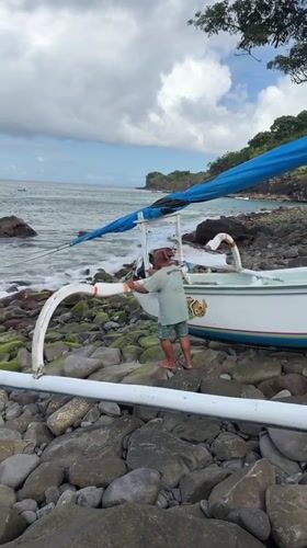 Man tends to beached outrigger boat on Indonesian shore