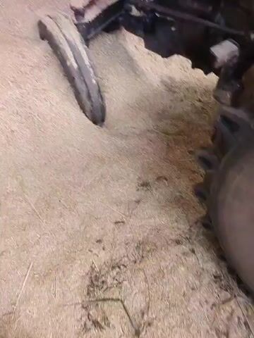 A close-up, shaky video shows the front wheel of a red tractor stuck in what appears to be loose straw or hay. The tire is sunk deeply into the material, creating a noticeable indentation. The tractor itself is partially visible, with the number "1035 D" clearly displayed on the side of the red hood. The ground beneath the straw is obscured. The video appears to have been filmed by someone standing close to the tractor.