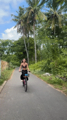 Woman rides pink bicycle through palm-lined Indonesian road