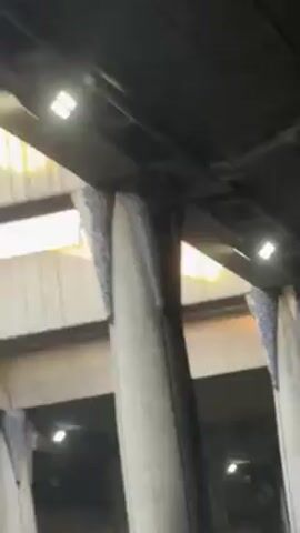 The video shows a low-angle view of concrete pillars supporting a structure overhead. The pillars have a flared design at the top where they meet the structure. There are small, square lights attached to the underside of the overhead structure. The lighting conditions are somewhat dim, and the camera appears to be moving slightly.