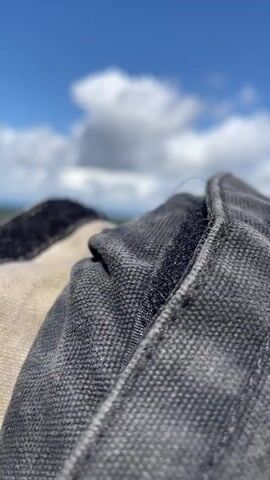 The video is a close-up, low-angle shot of climbing equipment against a backdrop of a blue sky with scattered clouds. The equipment appears to be a rope and harness system. The camera pans slightly to the right, revealing more of the ropes and a textured, weathered surface that could be a rooftop or ledge. In the distance, buildings and a hazy landscape are visible. The overall impression is of an outdoor setting with preparations for or completion of an activity that involves heights. There are no people clearly visible in the video.