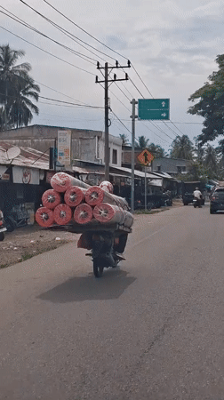 Motorcycle transports carpet rolls through Indonesian towns early morning
