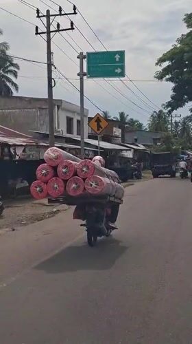 Motorcycle transports carpet rolls through Indonesian towns early morning