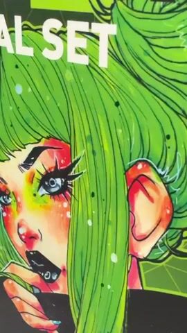 This media file shows a close-up of a box of "ART KOMPOZIT PROFESSIONAL SET ACRYLIC ART PAINTS." The box features a vibrant, stylized illustration of a person with bright green hair styled in pigtails, large expressive eyes with dramatic makeup, and pale skin with colorful accents. The person is depicted with a hand near their mouth, and their expression is ambiguous, possibly conveying surprise or intensity.

The box itself is predominantly black with green and white text. Visible text includes "ART KOMPOZIT," "PROFESSIONAL SET," "ACRYLIC ART PAINTS," and "NAL SET." Below the "ACRYLIC ART PAINTS" title, a grid displays swatches of various paint colors with their corresponding numbers and names. Examples of visible paint colors and names include "018 Titanium White," "116 Yellow Primary," "131 Ochre Yellow," "256 Crimson Red," "359 Red Permanent," "321 Light Green," "356 Deep Green," "378 Dark Green," "492 Brown," "390 Ultramarine Blue," and "440 Violet."

The camera pans slightly, revealing the side of the box and the spines of additional boxes stacked next to it. The lighting is bright and even, suggesting an indoor setting, possibly a retail store or an art supply storage area. The overall impression is one of vibrant art supplies, with the striking illustration on the packaging drawing immediate attention. The location context of Deerfield Beach, United States of America, is provided but not directly observable within the visual content of the media. No specific time of day or weather conditions are discernible. The dominant emotion conveyed by the illustration is one of boldness and artistic flair.