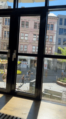 Window view onto a busy Linz street with a clock tower