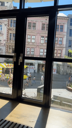 Window view onto a busy Linz street with a clock tower