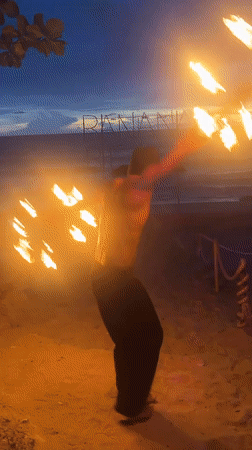 Fire performers and a flaming sign light up Banana Beach at dusk
