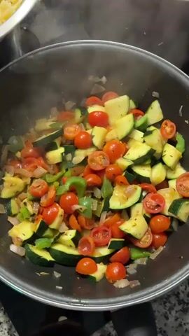The video shows multiple cooking activities taking place simultaneously. The first shot shows vegetables, specifically zucchini, cherry tomatoes, and green peppers, being sauteed in a large pot. Steam rises from the pot, indicating the food is hot and freshly cooked. The next shot reveals cooked farfalle pasta in a metal strainer, and an out-of-focus bowl of what appears to be additional pasta. The final shot features ground meat, possibly beef, being browned in a pan, with someone using a spatula to break it up. The video suggests the preparation of a pasta dish with meat and vegetables.