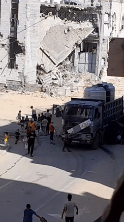 Water distribution at a truck amid heavy urban damage in al-Qarara