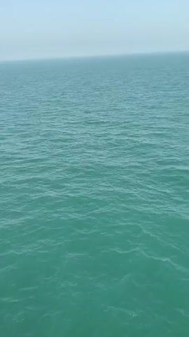 The video shows a vast expanse of teal-colored water under a hazy blue sky. The water has small ripples and waves, suggesting a gentle breeze. The horizon line is clearly visible, separating the water from the sky. There are no visible boats, landmasses, or other objects in the frame. The camera appears to be relatively stationary, possibly mounted on a boat or a high vantage point overlooking the sea. The overall impression is one of serene, open water.