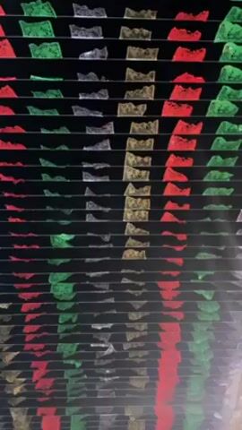 The video shows a view looking upward at rows of colorful paper decorations. The rows alternate in color, featuring green, silver, gold, and red paper cutouts. The decorations hang from a dark or black ceiling. The camera gradually pans upward, revealing more rows of decorations. No people are visible.