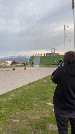 Skateboarder attempts jump trick in Ushuaia park on cloudy day
