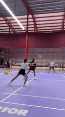 Doubles badminton match in progress on a purple indoor court