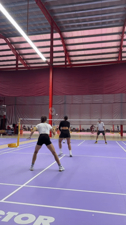 Doubles badminton match in progress on a purple indoor court