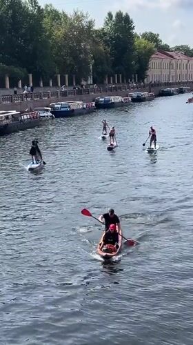 Costumed paddleboarders cruise a Saint Petersburg canal in summer.