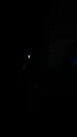 The video shows a person in a dark room. The person is wearing a hooded sweatshirt and sitting on a chair. A projector is displaying text onto a wall. The person is wearing glasses. The text appears to be in reverse.