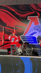 Band performs in red outfits with logo backdrop