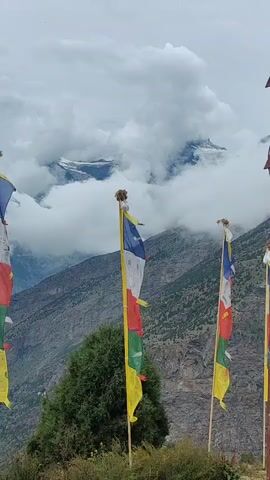 A video shows prayer flags on a mountain landscape. The flags are colorful and blow in the wind. In the background, there are mountains and clouds. The sky is cloudy.