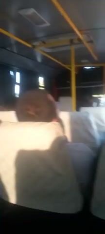 The video shows the interior of a bus. The camera is pointed towards the back of the bus, showing several passengers seated. The seats appear to be covered in a light-colored fabric. Yellow grab poles are visible, along with the ceiling of the bus. The lighting suggests it is daytime, with sunlight coming through the windows on the side. The video is shaky, indicating movement.