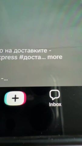 A person is filming a smartphone screen that is displaying a social media video. The smartphone itself has a visible crack running across its screen. The video on the phone shows a young woman performing a quick outfit change.

Initially, the woman is seen wearing a red two-piece lingerie set, consisting of a bra and thong, with a choker. Her long dark hair is down. The background appears to be the inside of a washing machine or a circular frame resembling one.

Mid-clip, there's a rapid movement where the woman changes her attire. She then appears in a black long-sleeved top and a red skirt, holding up the black top. The washing machine background remains consistent.

The phone screen also displays several elements typical of a social media platform (likely TikTok):
- At the top, "17:40" is visible, along with navigation options "Explore Following For You."
- To the right of the video, there are engagement metrics: a heart icon with "136.2K" (likes), a comment icon with "600" (comments), a bookmark/save icon with "24K" (saves), and a share icon with "102.6k" (shares).
- Below the video, partially visible text from the original video caption reads "o на доставките - xpress #досTa_ more", which translates to "on deliveries - [Ali]express #deliv_ more".
- At the very bottom of the phone screen, there's a navigation bar with icons including a "+" button, "Inbox," and "Profile."

In the background of the actual video recording (behind the phone), a light-colored table is visible. On the table, there is a white bowl, possibly containing cereal or popcorn, and a clear drinking glass. The overall lighting suggests an indoor, daytime setting.