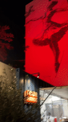 Red-lit ballerina mural on an Athens building at night