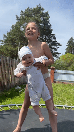 Girl and baby play on trampoline in Russian backyard