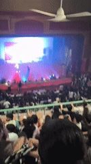 Lit stage and tiered audience at a Dharamshala indoor event