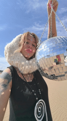 Woman holds disco ball in sandy area near Chaikovsky