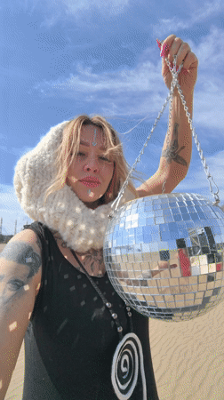 Woman holds disco ball in sandy area near Chaikovsky