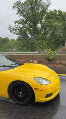 Yellow Corvette drives wet highway during rainy evening