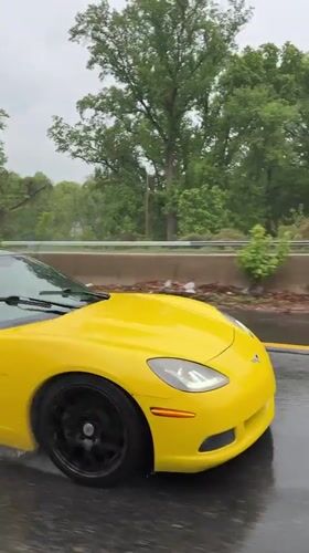 Yellow Corvette drives wet highway during rainy evening
