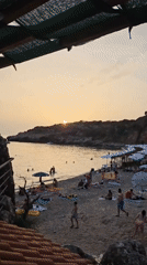 Crowded pebble beach soaks up a golden-hour sunset