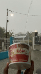 Person holds instant meal container during heavy rainfall in Indonesia