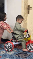 Girl pushes toddler on tricycle in Quetta, Pakistan