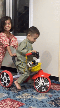 Girl pushes toddler on tricycle in Quetta, Pakistan