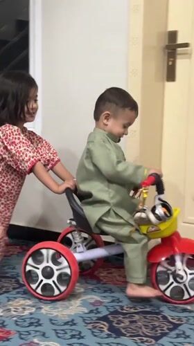 Girl pushes toddler on tricycle in Quetta, Pakistan