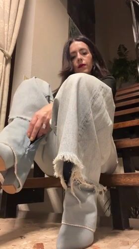 Woman adjusts denim boot while sitting on bench in Konz
