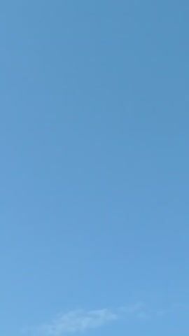 The video shows a clear blue sky with a few wispy clouds. A small airplane is visible in the distance, flying from left to right. The airplane is small and appears to be at a high altitude.