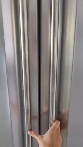 A person's right hand opens the left door of a stainless steel, double-door refrigerator. The interior reveals several shelves filled with various food items. On the main shelves, there are plastic-wrapped packages of food, multiple containers, jars, and cartons of eggs. The refrigerator's internal light is on, illuminating the contents. The person then opens the right door, which holds multiple bottles, appearing to be beverages like beer, in door compartments. On the lowest shelf of the right door, a bottle of "Fuze Tea" is visible. The refrigerator appears well-stocked.