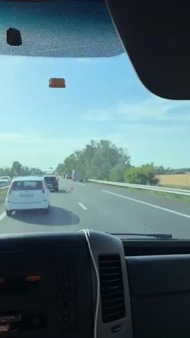 The video shows a traffic jam on a highway. Several emergency vehicles, including a fire truck and a tow truck, are present. There are also police cars and traffic cones on the road. People in high-visibility vests are visible, appearing to be emergency responders directing traffic or working at the scene of an incident. The weather appears to be sunny.